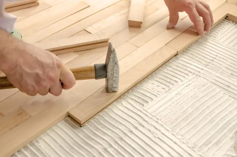 Handwerker verlegt Parkettboden, indem er Holzdielen mit einem Hammer festsetzt.