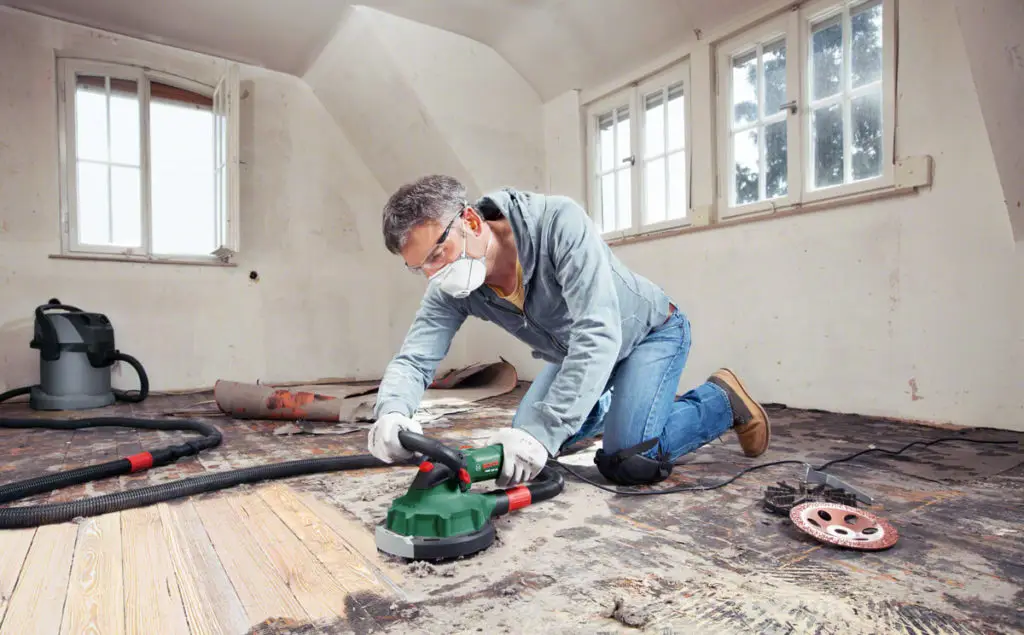 Mann mit Schleifgerät bei der Renovierung eines alten Holzbodens, um ihn für die weitere Bearbeitung vorzubereiten.